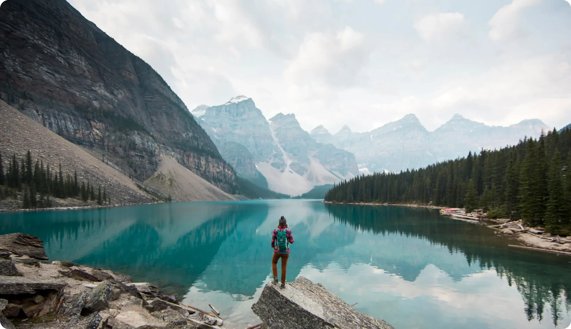 A person hiking standing in front of a blue lake with mountains reflecting in it